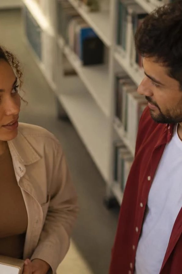 Duas participantes de pé conversando no corredor entre prateleiras de livros